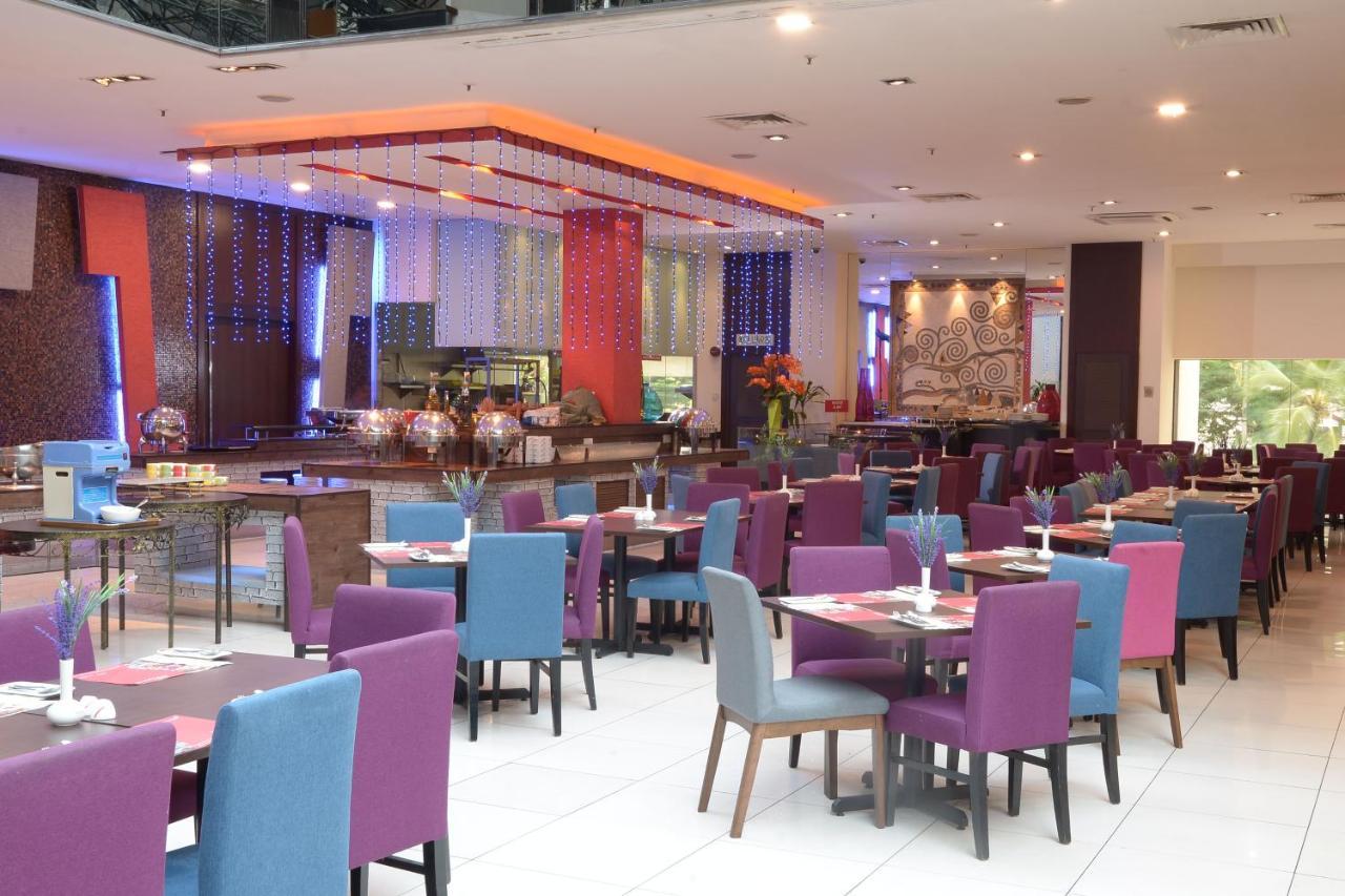 Seri Pacific Hotel Kuala Lumpur Exterior photo The photo shows the interior of a restaurant. It features a spacious dining area with a mix of purple and blue chairs arranged around wooden tables. The setting is modern and colorful, with bright lighting and decorative elements such as floral arran