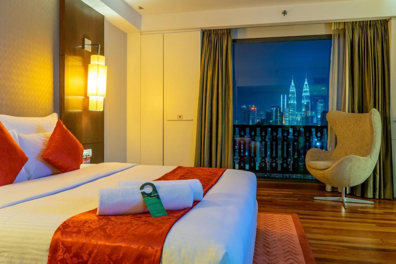 Seri Pacific Hotel Kuala Lumpur Exterior photo The photo shows a stylish hotel room with a modern design. It features a large bed with white linens and decorative orange accents, along with two pillows. There is a plush armchair in a contemporary style and large windows covered with curtains, off