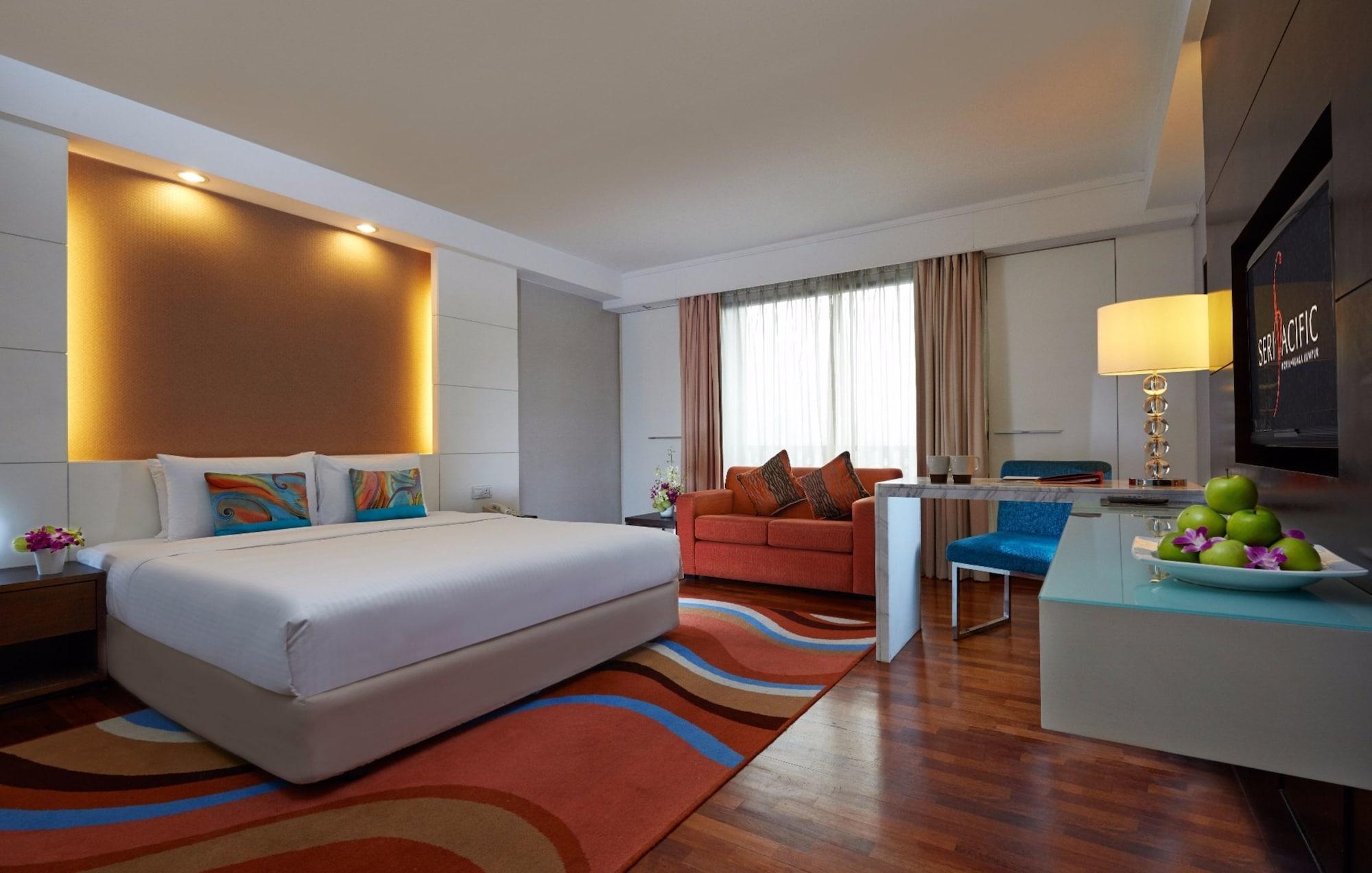 Seri Pacific Hotel Kuala Lumpur Exterior photo The image shows a well-decorated hotel room. On one side, there is a large bed with a light-colored headboard, complemented by colorful pillows. A cozy orange sofa is positioned across from the bed, creating a comfortable seating area. There is a mod