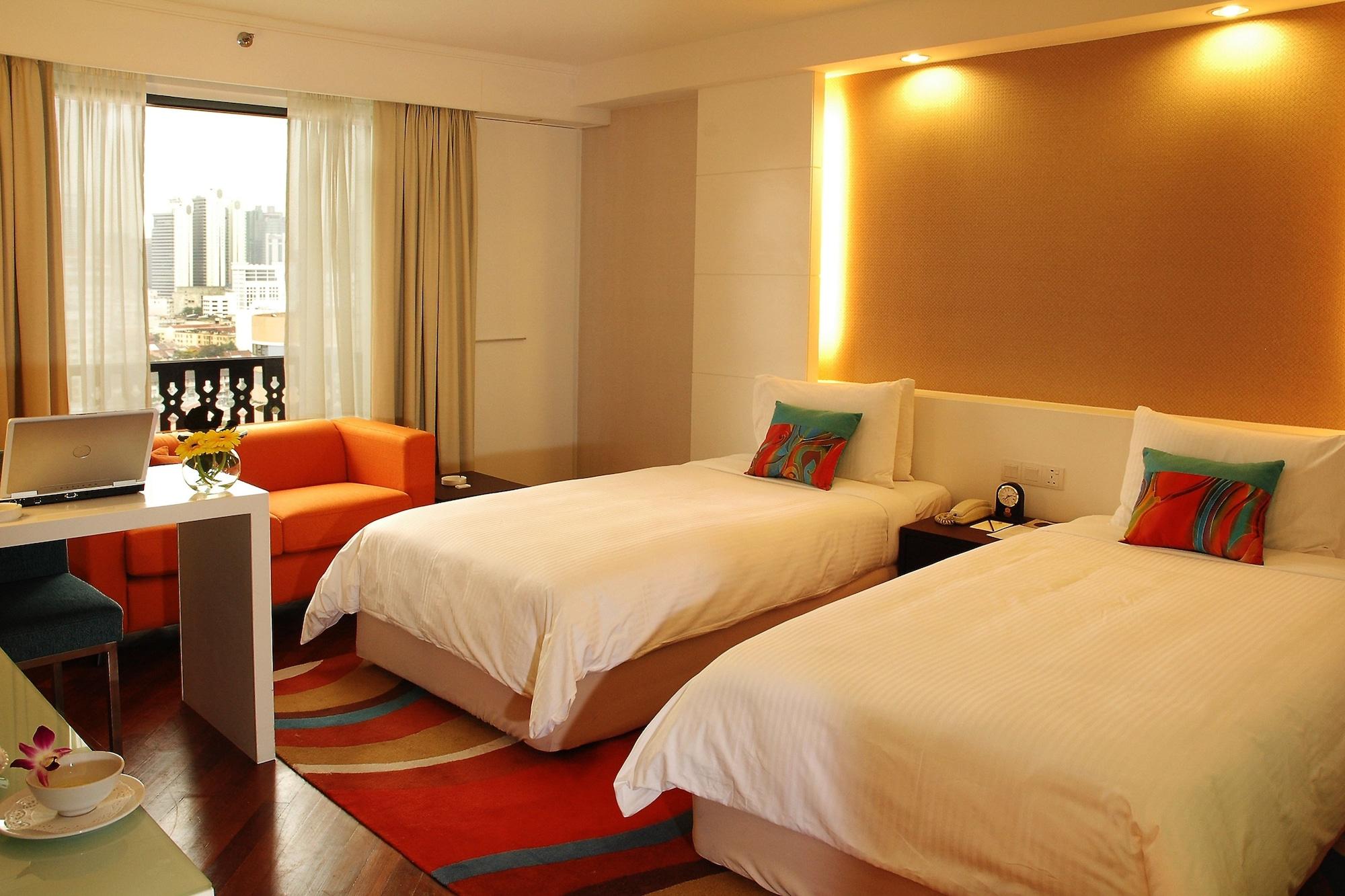 Seri Pacific Hotel Kuala Lumpur Room photo The photo shows a modern hotel room featuring two single beds with white bedding. There is a cozy orange sofa in one corner and a small table with a laptop on it. The room has large windows with curtains that allow natural light to brighten the space