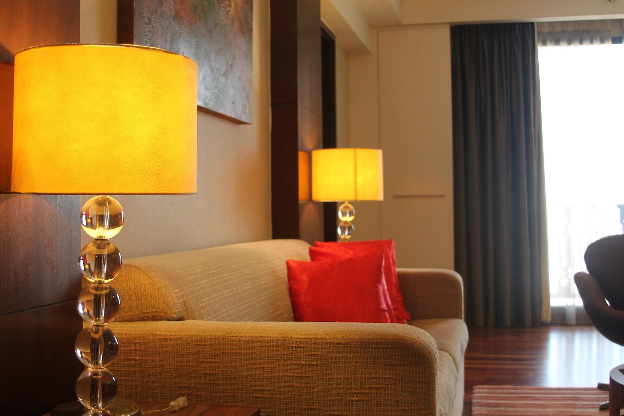 Seri Pacific Hotel Kuala Lumpur Exterior photo The photo shows a cozy interior space, featuring a light-colored sofa and two decorative lamps with yellow shades. One lamp is placed next to the sofa, highlighting the area. A bright red pillow is resting on the sofa, adding a pop of color. The wall