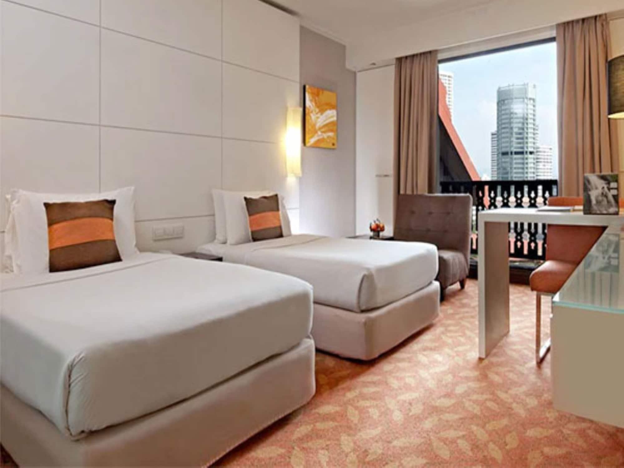 Seri Pacific Hotel Kuala Lumpur Exterior photo The photo shows a contemporary hotel room featuring two twin beds with light-colored bedding and decorative pillows. There's a small seating area with an armchair, and a desk with a clear top. Large windows allow natural light to enter, providing a v