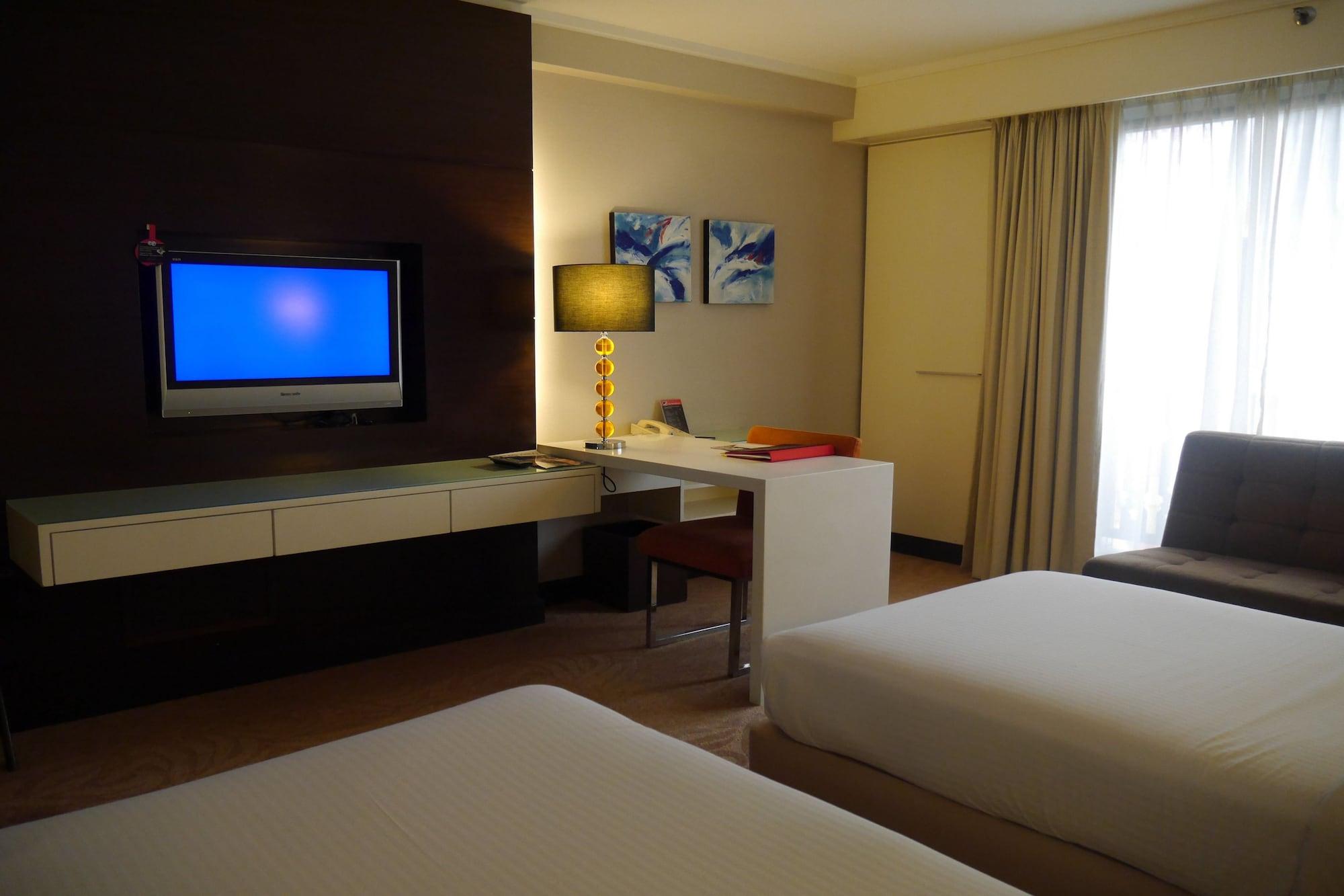 Seri Pacific Hotel Kuala Lumpur Exterior photo The photo shows a modern hotel room featuring two beds with white linens. There is a flat-screen TV mounted on the wall in front of the beds. Next to the TV, there is a desk and a chair, along with a lamp. The room has light-colored walls and curtain