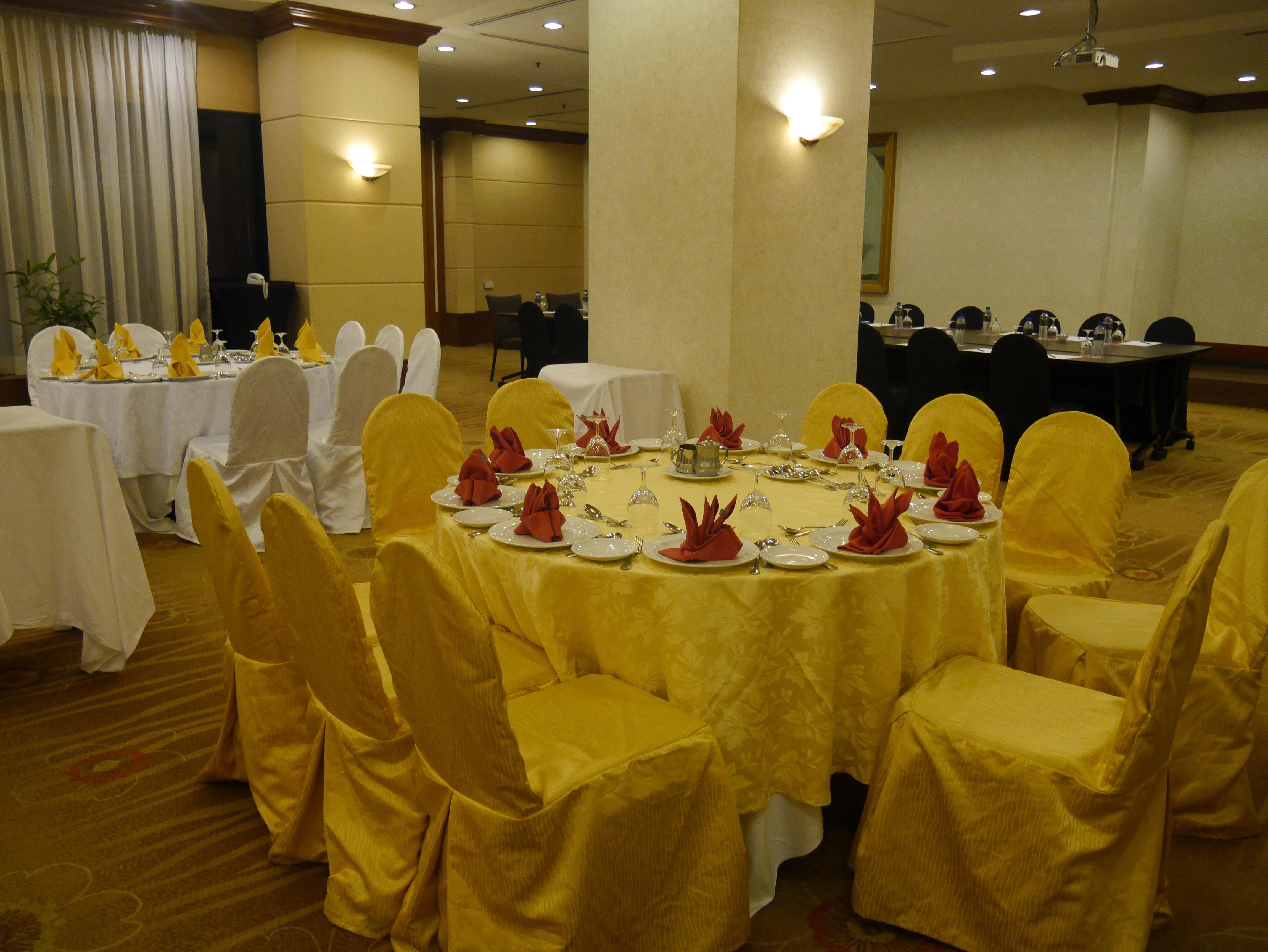 Seri Pacific Hotel Kuala Lumpur Exterior photo The photo shows a banquet or dining area set up for an event. There are several tables covered with white and yellow tablecloths. The table in the foreground features chairs with yellow covers and is adorned with neatly arranged plates, utensils, and