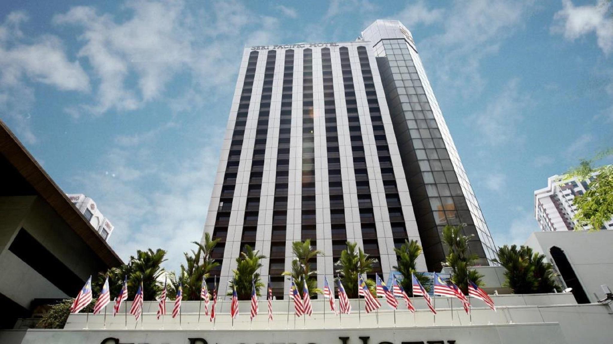 Seri Pacific Hotel Kuala Lumpur Exterior photo The photo shows a tall modern building with a predominantly glass facade. The structure has a sleek design and appears to be several stories high. In the foreground, there are multiple flags on display, likely representing the United States, as they 