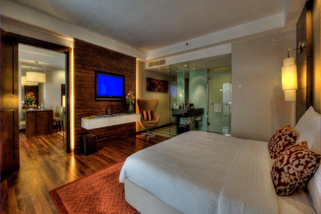 Seri Pacific Hotel Kuala Lumpur Exterior photo The photo shows a modern hotel room featuring a large bed with white linens and decorative pillows. There is wood flooring and an area rug in front of the bed. A flat-screen television is mounted on the wall, and next to it is a stylish wooden dresse