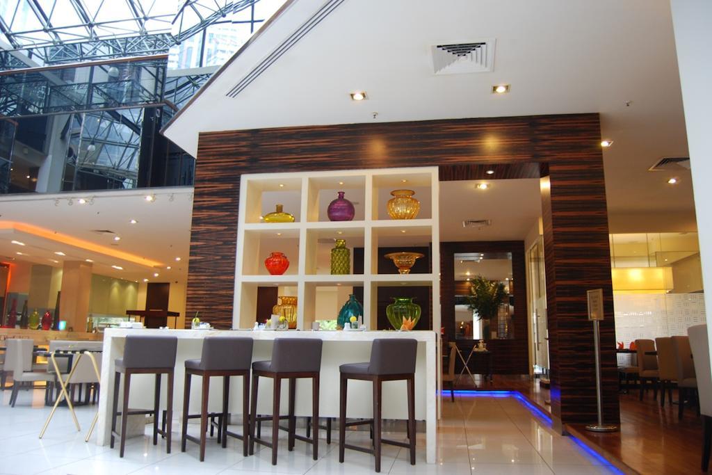 Seri Pacific Hotel Kuala Lumpur Exterior photo The image shows an interior space, likely a modern restaurant or hotel lobby. There is a sleek bar area with several high stools arranged in front of a stylish back counter. Behind the bar, there are several shelves displaying colorful glassware and 